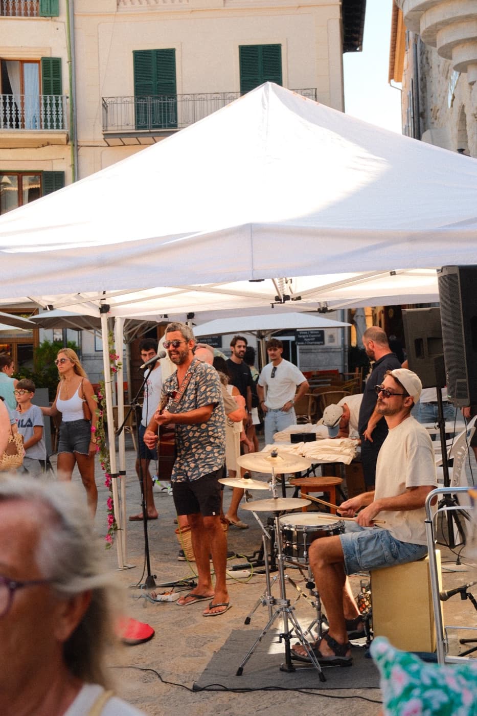 A band playing under a canopy in a town square, with a crowd watching
