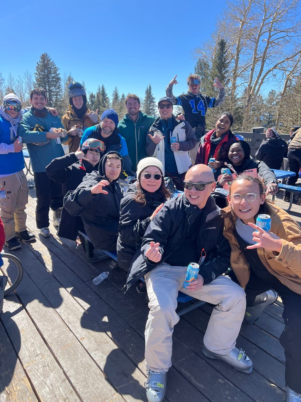 A big group in ski gear crowded round a picnic table on a sunny deck in Flagstaff